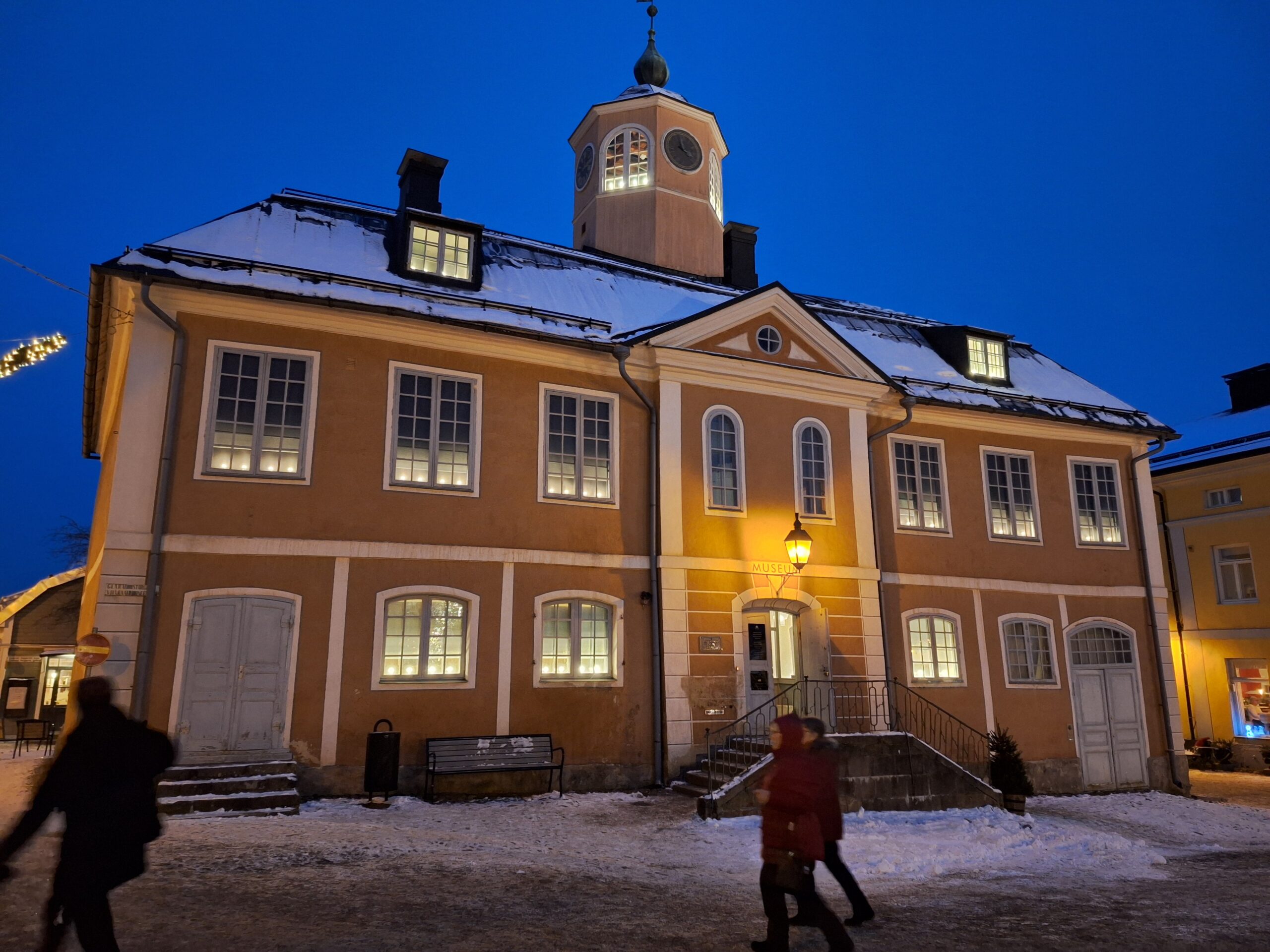 Kuva Porvoon vanhasta raatihuoneesta jouluna, lumisessa iltamaisemassa. Ihmisiä kävelee raatihuoneen ohi.