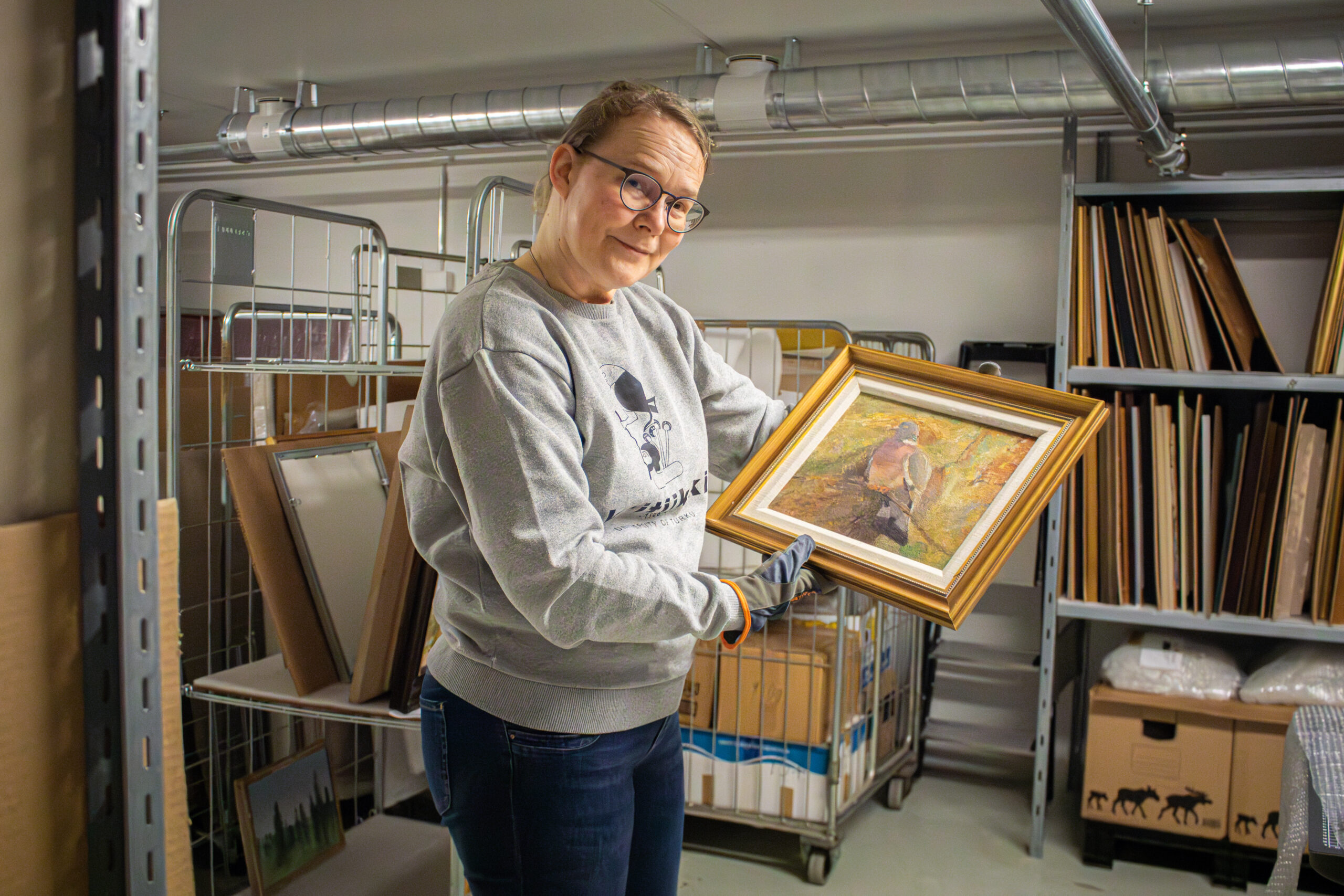 Amanuenssin sijainen Mariaana Korpela pitelee kädessään teosta ja katsoo hymyillen.