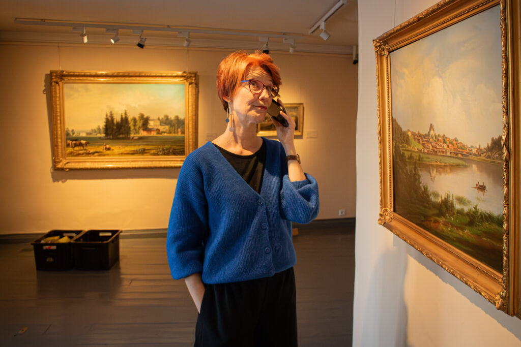 Wahlström talar i telefon i ett rum med landskapsmålningar.