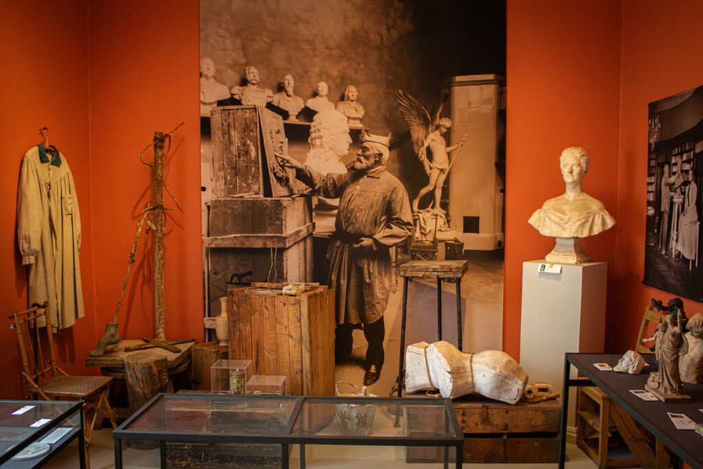 På bilden syns ett av rummen i utställningen med Walter Runebergs skulptursamling. Rummet har en rödaktig ton och där visas bland annat ett porträtt av Runeberg. I rummet finns också arbetsredskap som han använde i sitt arbete.