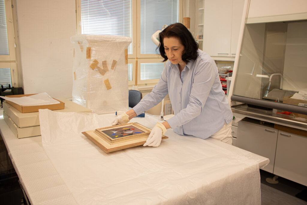 Jordas packar en oljemålning i silkespapper vid ett bord i museets konserveringsutrymmen.