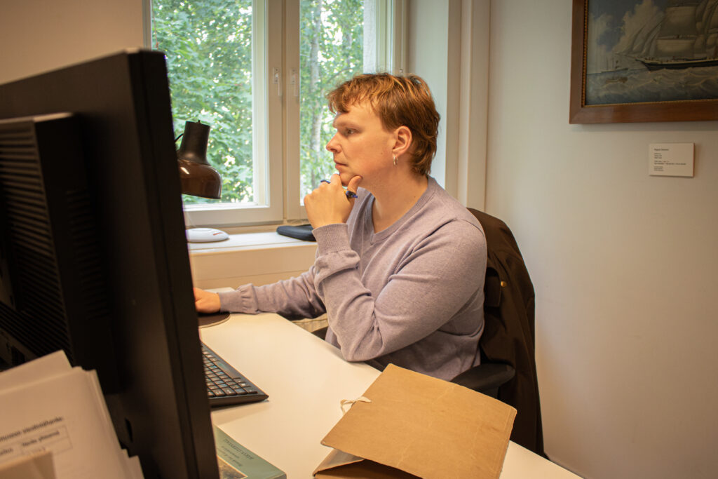 Olli Järveläinen sitter på en svart stol vid sin arbetsplats framför datorn.