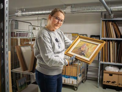 Amanuenssin sijainen Mariaana Korpela pitelee kädessään teosta ja katsoo hymyillen.